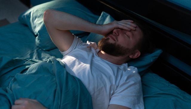 View of a man waking up uncomfortably with his hand over his face in bed