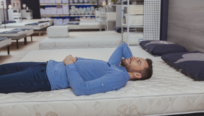 A man lays on his back in a mattress showroom.