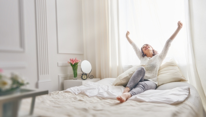 A woman sits happily on her freshly made bed.