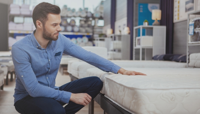 A man presses down on a mattress in a showroom as he looks for a new mattress.