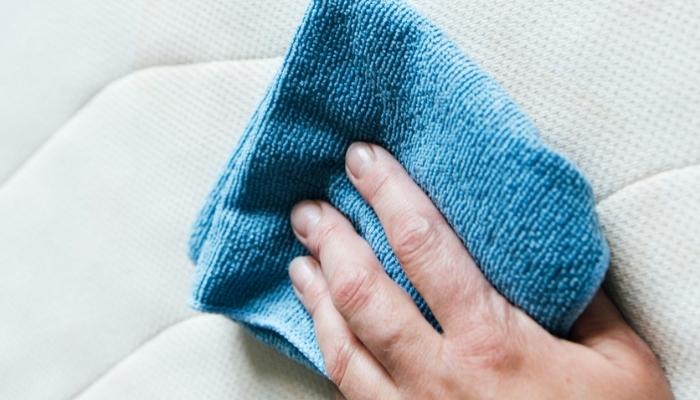 hand using cloth to clean mattress