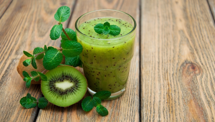 A glass of kiwi juice with a couple kiwis next to it