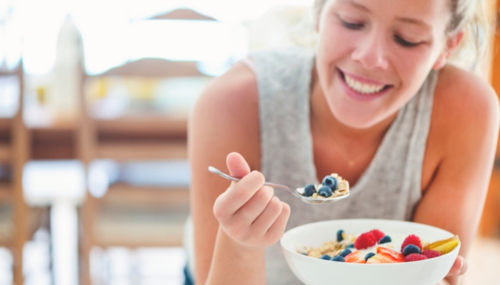 Woman eating a bowl of yogurt with fruit and grain toppings
