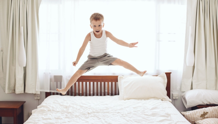 A young boy in pajamas jumps on a white bed.