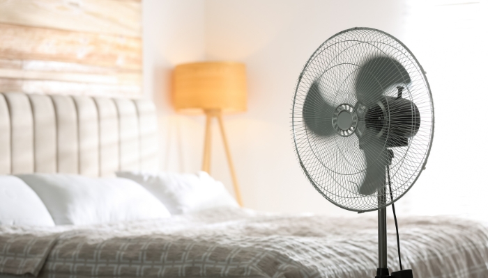 An electric fan runs next to a bed.