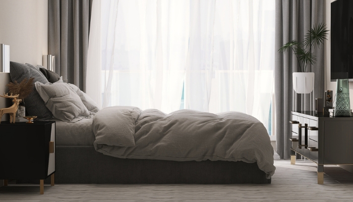 A bed sits in front of an open window with blackout curtains.
