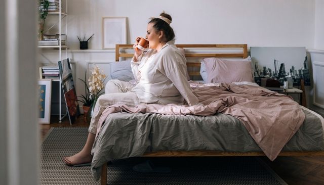 view of a woman sitting on a bed with the correct size frame drinking coffee