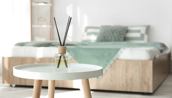 Closeup of a reed diffuser on a table in front of a bed