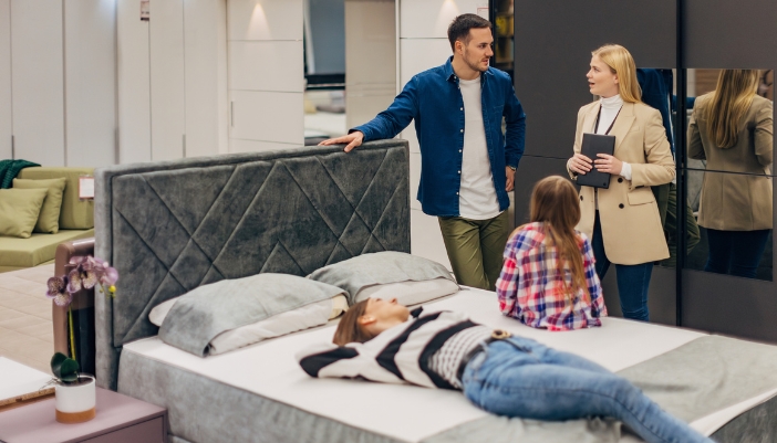 A couple and their child are testing mattresses and talking with a store employee