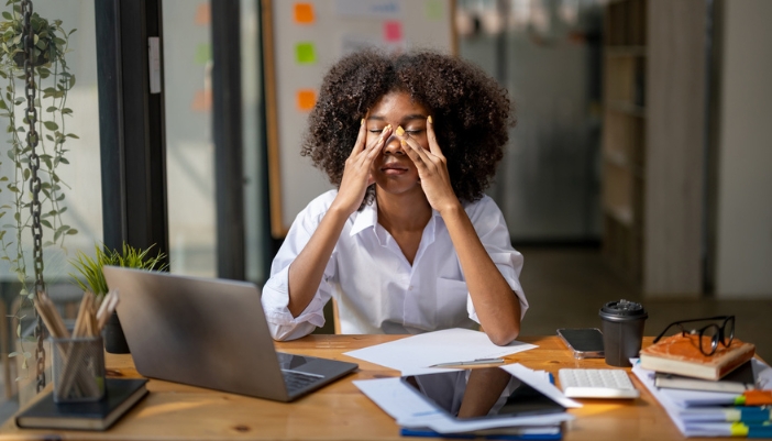 A woman rubs her forehead with a headache at her desk.