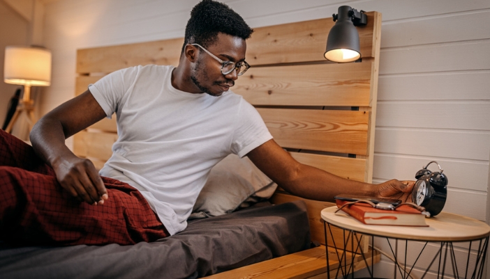 A man settles into bed for the night and sets an alarm.