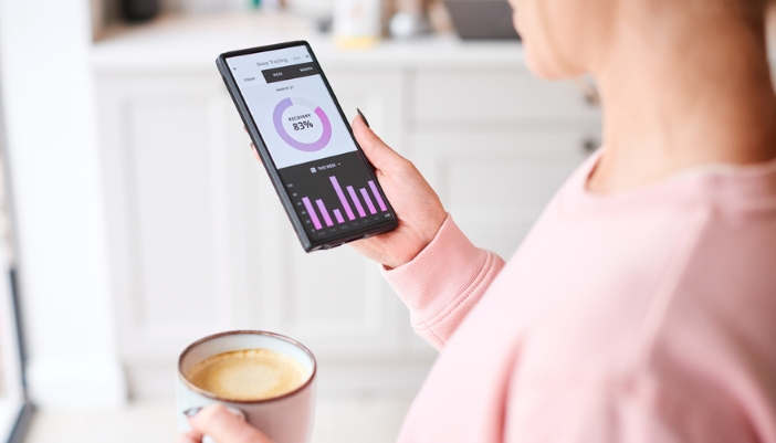 A woman drinks coffee and looks at her sleep tracking app on her smart phone.