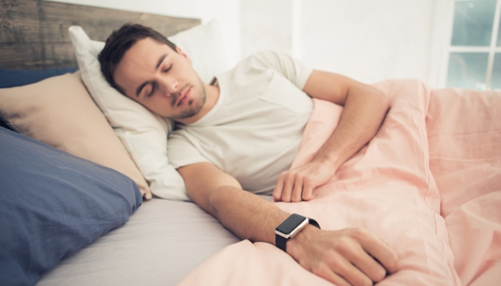 A man sleeps in bed with a smart watch on his arm.