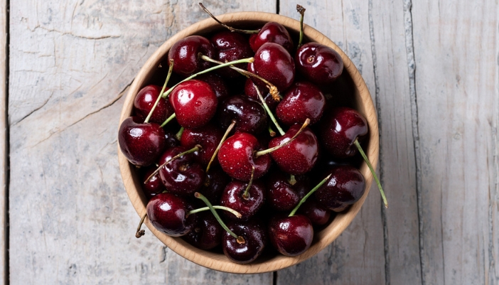 A bowl of ripe cherries sits on a slate background.