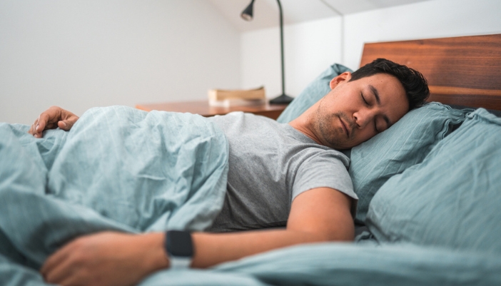 A man sleeps restfully in his darkened bedroom.