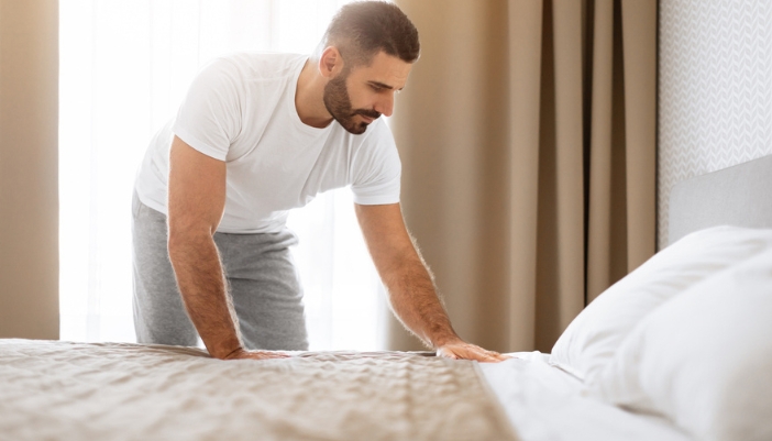 A man smooths out his comforter to finish making the bed.