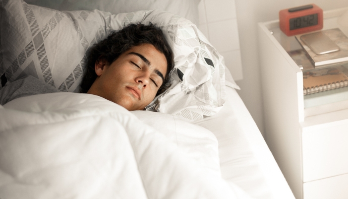 A teenage boy sleeps soundly in a bed with white bedding.