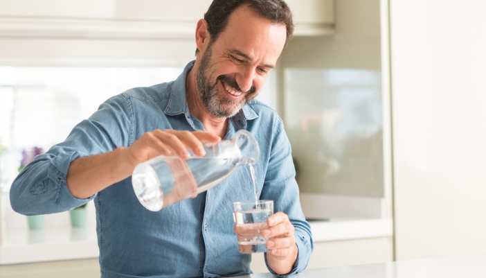 A middle-aged man pours himself a glass of water at home.