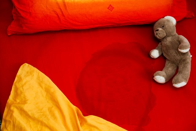 bed with red and yellow bedding with wet spot and teddy bear