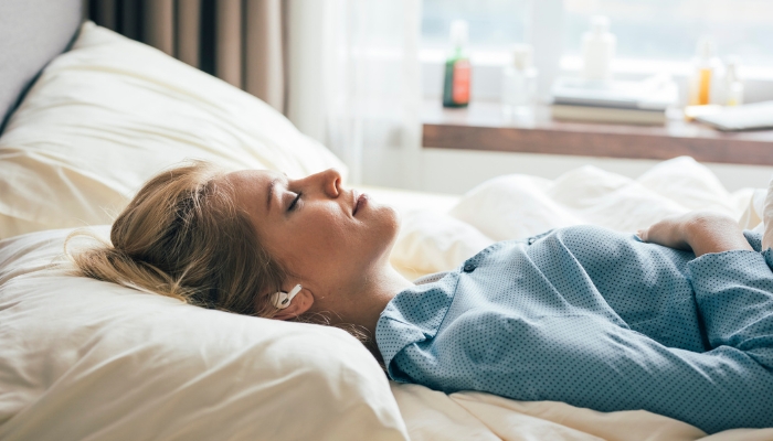 side profile shot of woman sleeping in bed while wearing bluetooth ear buds