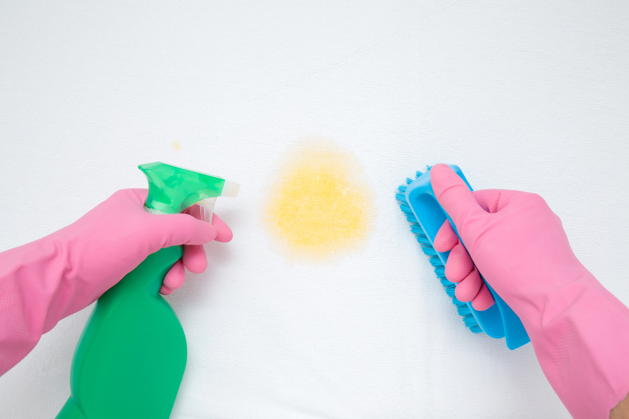 gloved hand cleaning stain with spray bottle and scrub brush