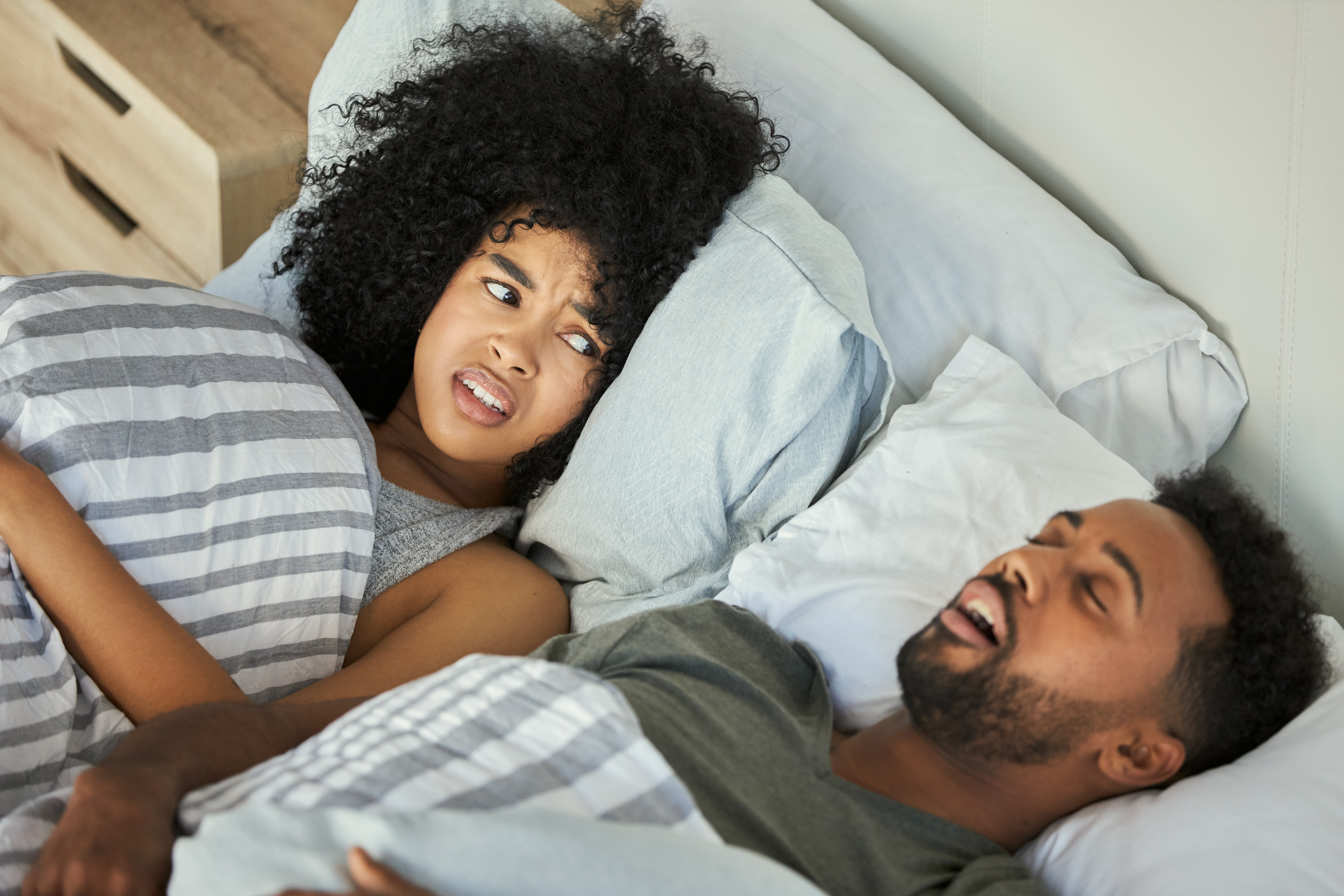 An irritated young woman looks at a man snoring in bed 