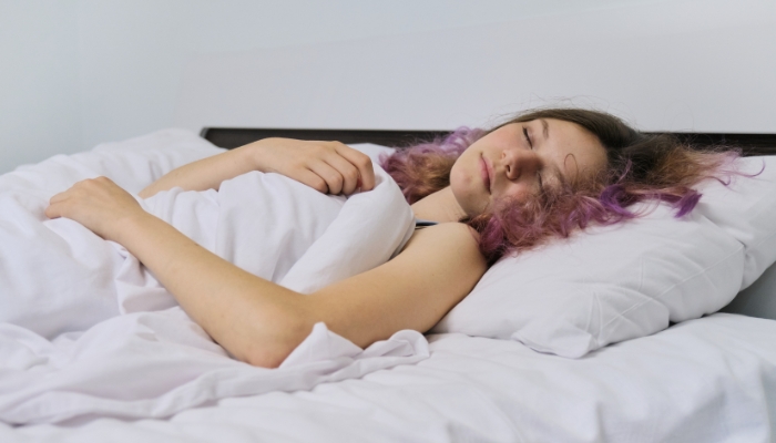 Older teen with purple streaks sleeping in a larger full or queen-size bed