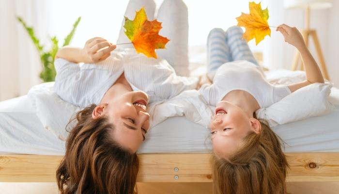 A woman and child lying upside down on a hybrid mattress holding fall leaves