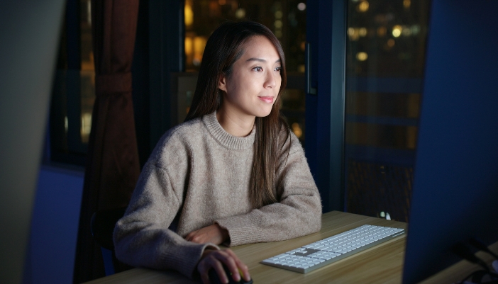 A woman workson her computer late at night, the monitor lights up her face.
