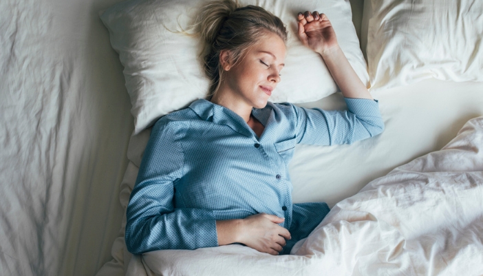 A woman in blue pajamas lays on a white bed sleeping.