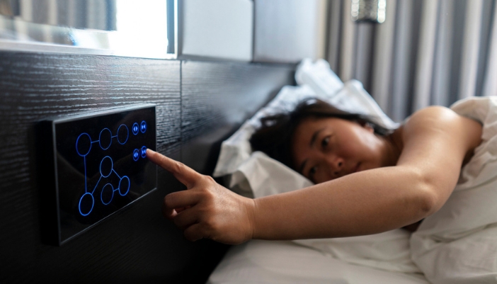 A woman adjusts an electronic tablet while laying in bed.
