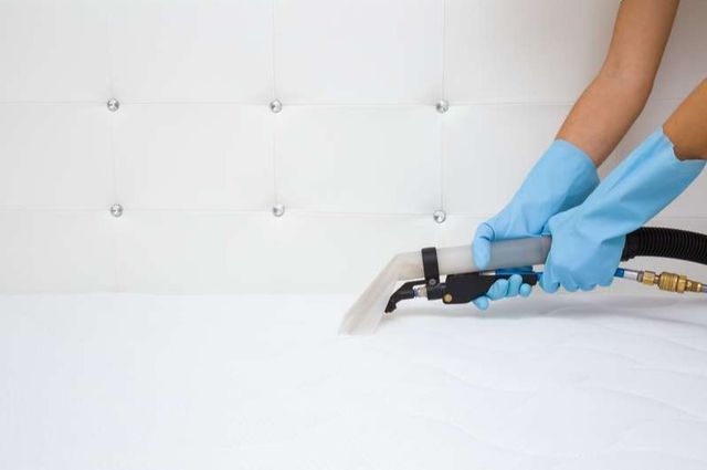 close view of two arms wearing gloves and vacuuming a white full size mattress