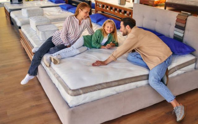 view of a family of three sitting on a mattress at a mattress store