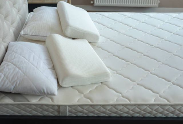 view of a white memory foam mattress with a white upholstered headboard and four white memory foam pillows on top