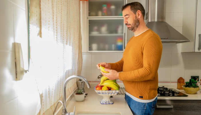 A man is peeling a banana in his kitchen