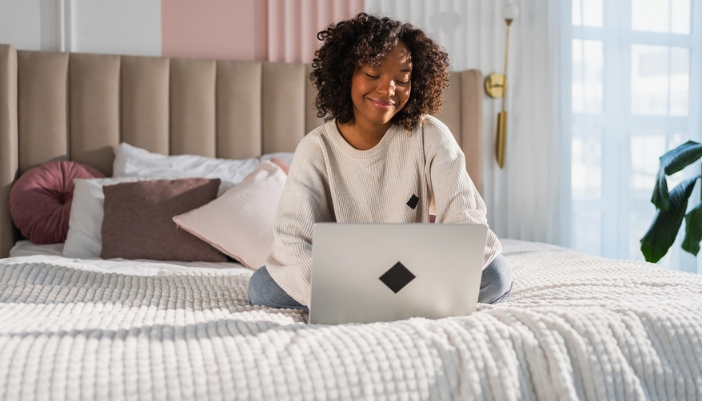 A woman sits on her bed using her laptop.