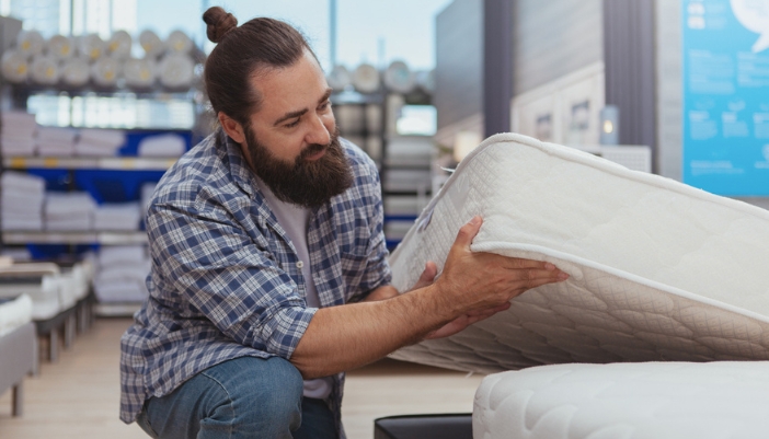 A man lifts a mattress off its frame in a mattress showroom.