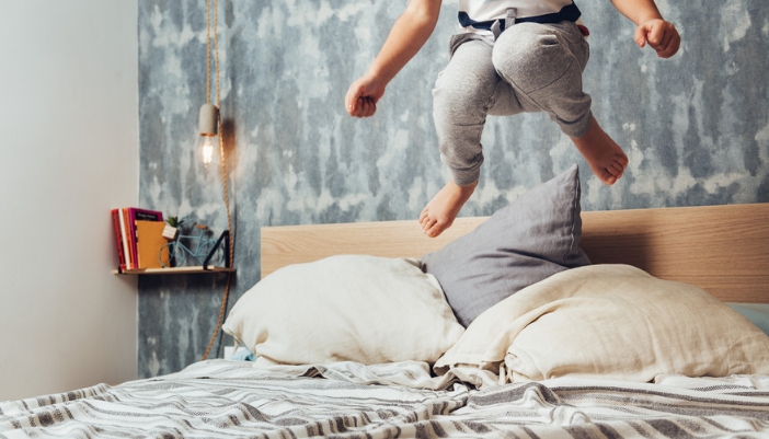 A young boy jumps on an unmade bed.
