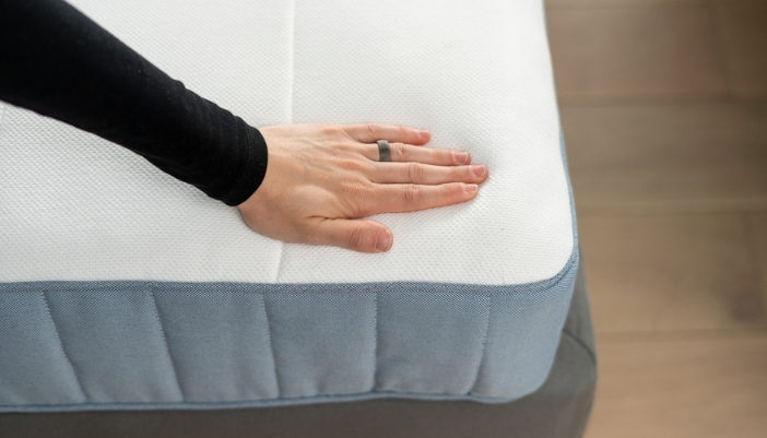 A hand presses down on a foam mattress.