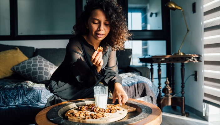 A woman sits on her couch eating nuts and drinking milk.