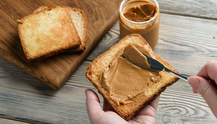 A hand spreads nut butter on a piece of toast.