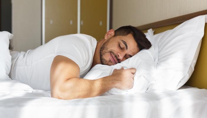 A man sleeps happily on a white pillow and sheet.