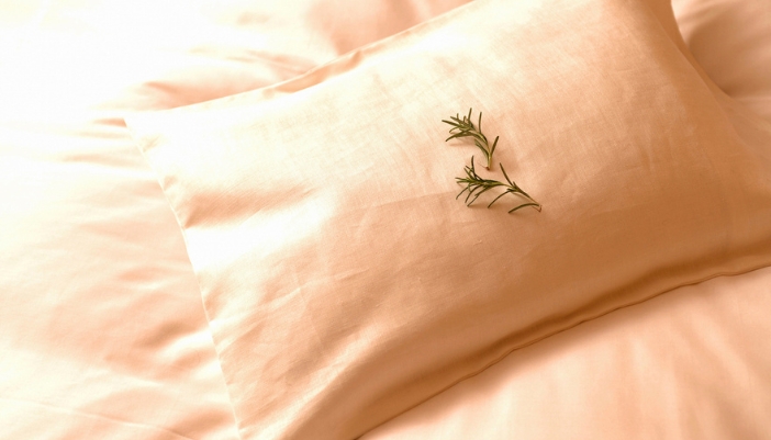 A pair of rosemary leaves rests on a bed’s pillow.