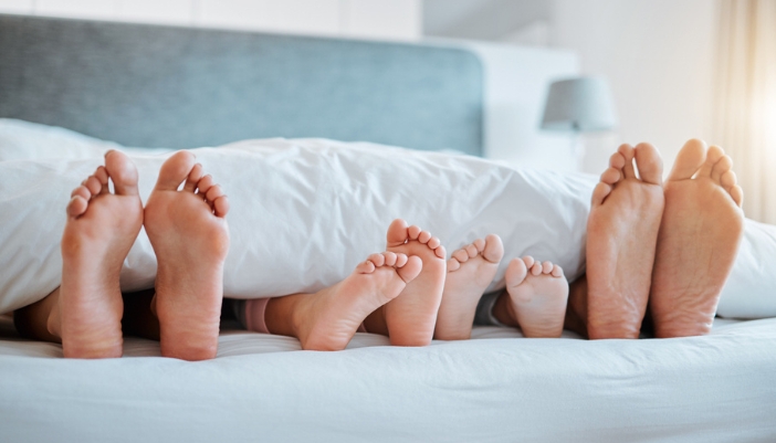 A family lays in bed with their feet facing out. 