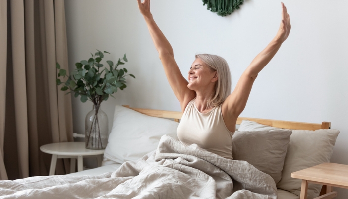 A woman wakes up happily and stretches her arms above her head.