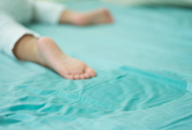 view of a wet spot on a bed next to a toddlers feet