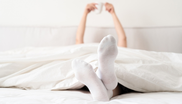A pair of female hands holds up a cup of coffee in the background with a pair of feet in the focus.