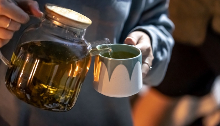 A closeup of a pair of hands pour a cup of tea into a cup.