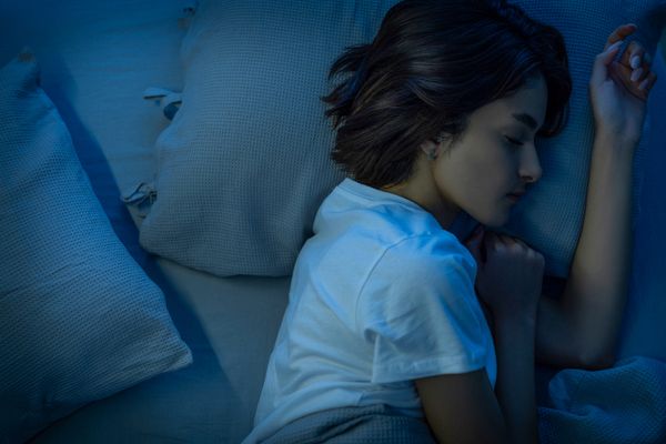 A blue filter over an overshot of a woman sleeping on her side 
