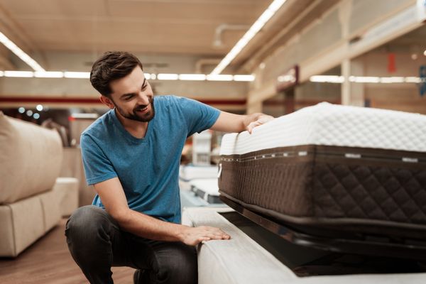 A smiling young man inspecting a mattress in a store